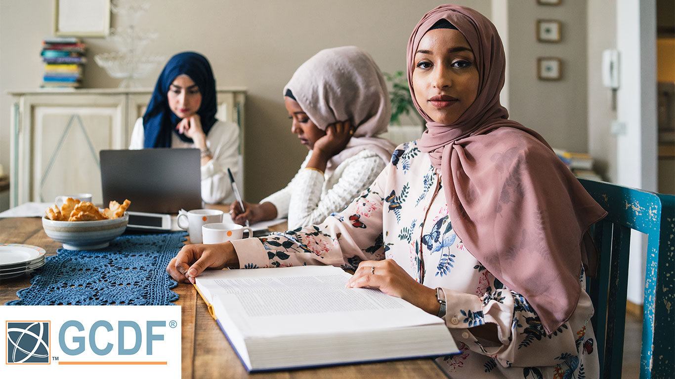 Three young Muslim women study on books and laptop at the kitchen table - Arabian millennials are preparing for university exams.